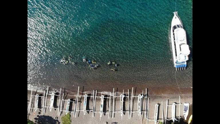Drone view of divers entering the water from Amed beach beside a row of jukung boats