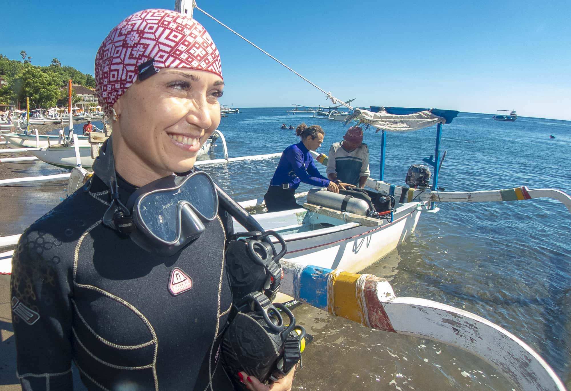 A smiling diver in a wetsuit on a jukung boat at the beach in Amed