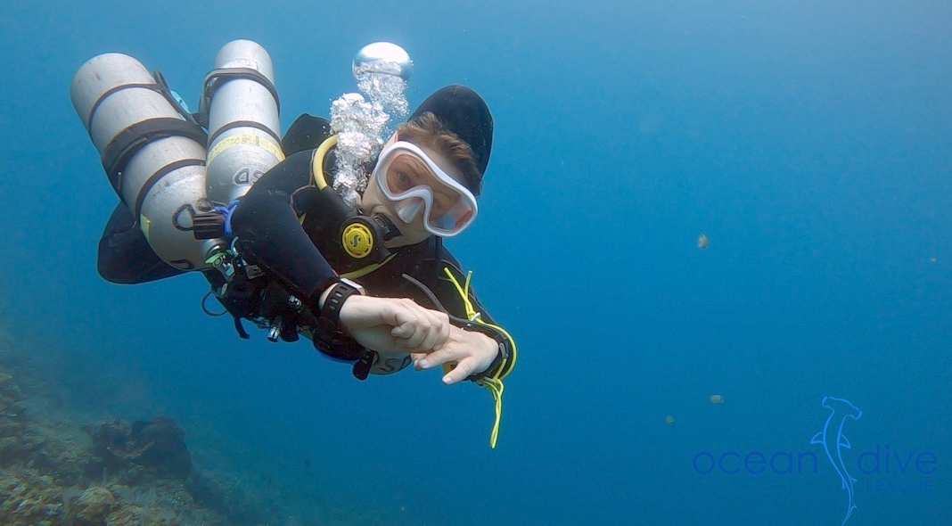 Sidemount diver in horizontal trim over the reef, signalling OK