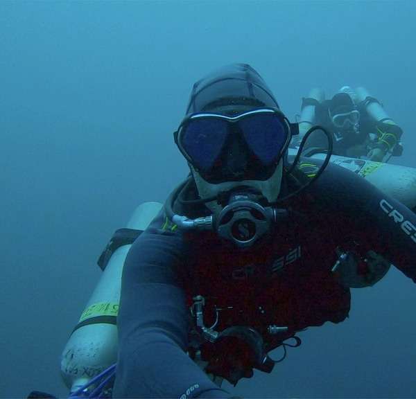 Technical diver with sidemount cylinders in deep blue water, a second diver behind